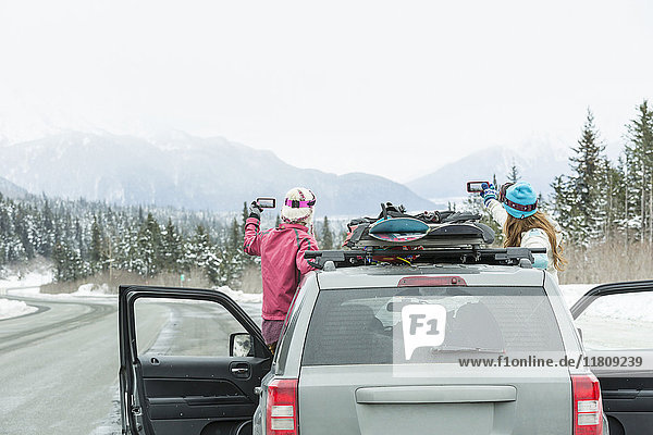 Kaukasische Frauen stehen im Auto im Winter fotografieren landschaftliche Aussicht
