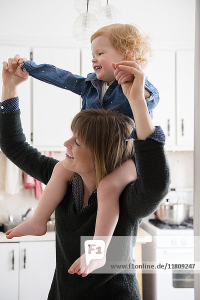 Caucasian mother carrying daughter on shoulders in kitchen