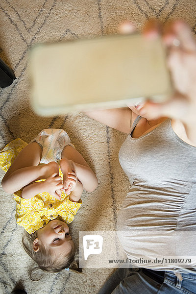 Schwangere Mutter macht Handy-Selfie auf dem Boden mit kaukasischer Tochter