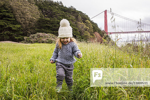 Caucasian girl running in grass near bridge