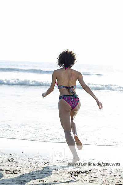 Gemischtrassige Frau im Bikini läuft zum Meer