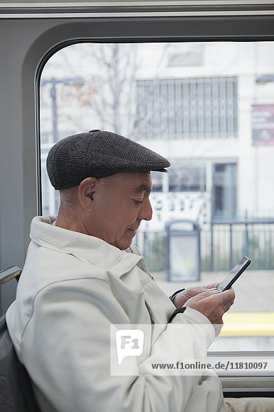 Hispanischer Mann sitzt im Zug und schreibt eine SMS mit seinem Handy