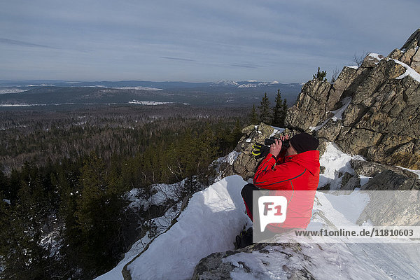 Kaukasischer Mann sitzt im Schnee und bewundert die malerische Aussicht auf den Wald