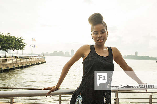 Porträt einer afroamerikanischen Frau  die sich an ein Geländer am Wasser lehnt