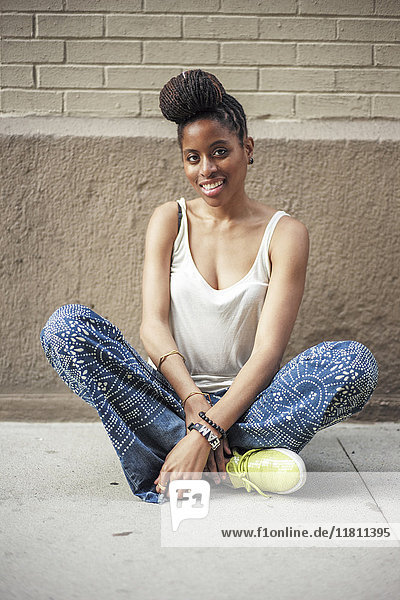 Lächelnde afroamerikanische Frau auf dem Bürgersteig sitzend