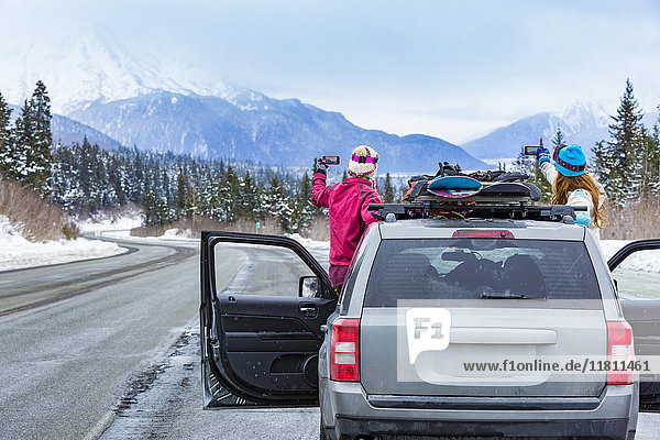 Kaukasische Frauen  die vom Auto aus mit Snowboards fotografieren