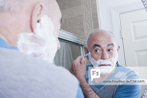 Reflexion eines hispanischen Mannes beim Rasieren des Gesichts im Spiegel