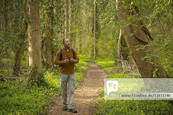 African American man walking on path in forest holding binoculars