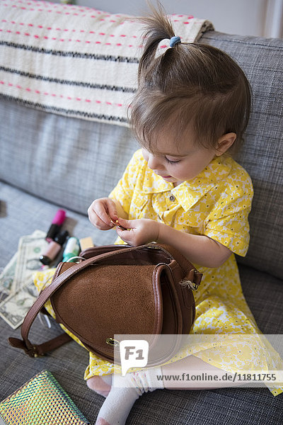 Kaukasisches Babymädchen spielt mit Handtasche auf Sofa