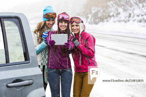 Women posing for selfie with digital tablet near car in winter