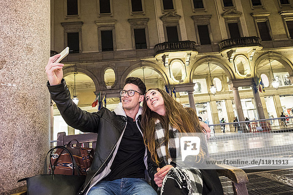 Caucasian couple sitting on urban bench posing for cell phone selfie