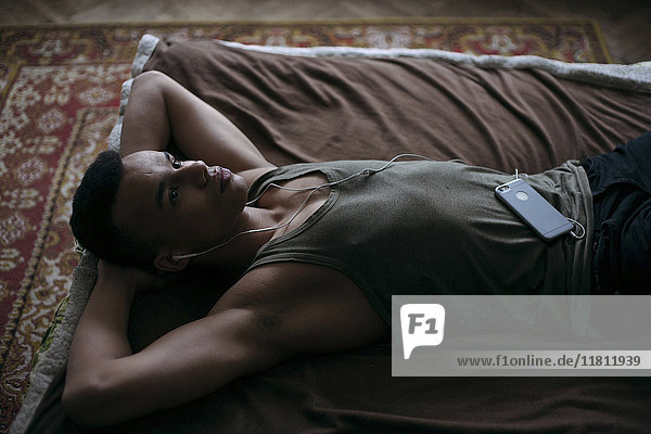 Black man laying on bed listening to music on cell phone