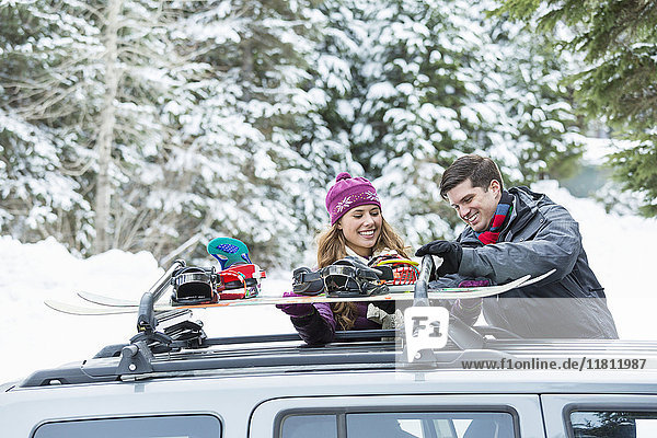 Kaukasisches Paar überprüft Snowboards auf dem Dachgepäckträger eines Autos