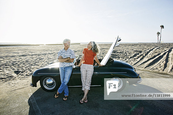 Älteres kaukasisches Paar lehnt an Cabrio mit Surfbrett am Strand