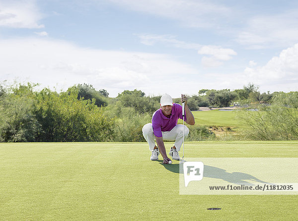 Hispanic golfer crouching on golf course