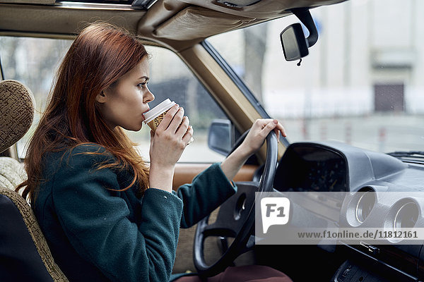 Kaukasische Frau fährt Auto und trinkt Kaffee