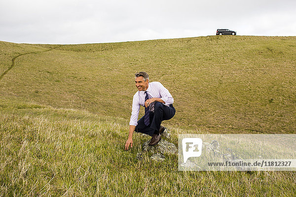 Smiling Caucasian businessman crouching in grass