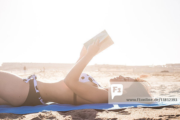Kaukasische Frau liegt auf einer Stranddecke und liest ein Buch