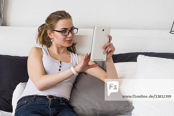 Kaukasische Frau sitzt auf dem Bett und benutzt ein digitales Tablet