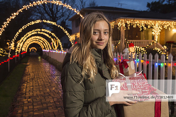 Kaukasisches Mädchen mit Weihnachtsgeschenken auf dem Bürgersteig