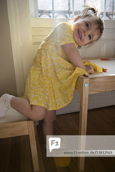 Porträt eines lächelnden kaukasischen kleinen Mädchens  das sich auf einen Tisch stützt