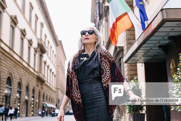 Reife Frau mit langen grauen Haaren mit Rollkoffer vor einem Hotel in Florenz  Italien