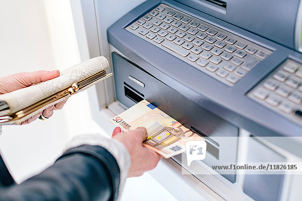 Hand einer Frau beim Abheben von 50-Euro-Scheinen am Geldautomaten