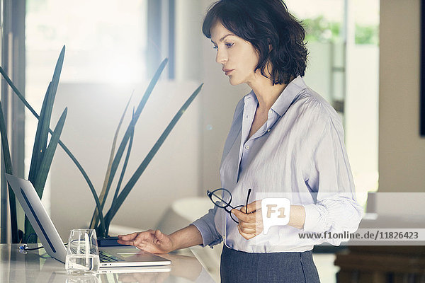 Reife Geschäftsfrau betrachtet Laptop in stilvollem Büro