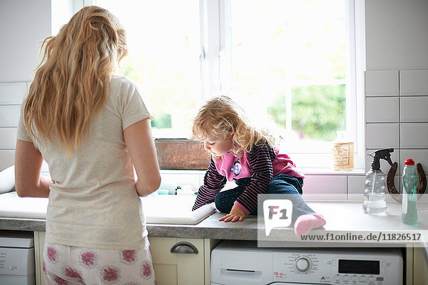 Mutter und Tochter in der Küche  Tochter sitzt auf der Arbeitsfläche und hilft der Mutter beim Abwasch