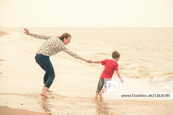 Junge zieht Mutter vom Strand ins Meer