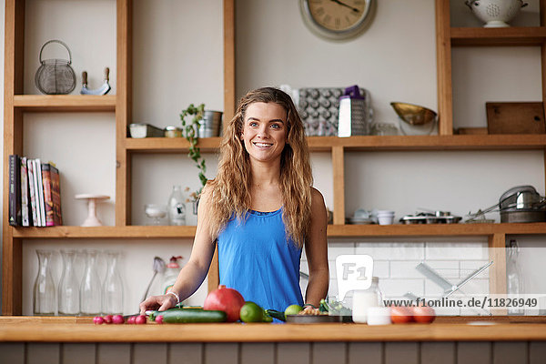 Glückliche junge Frau steht an der Küchentheke und bereitet Gemüse zu