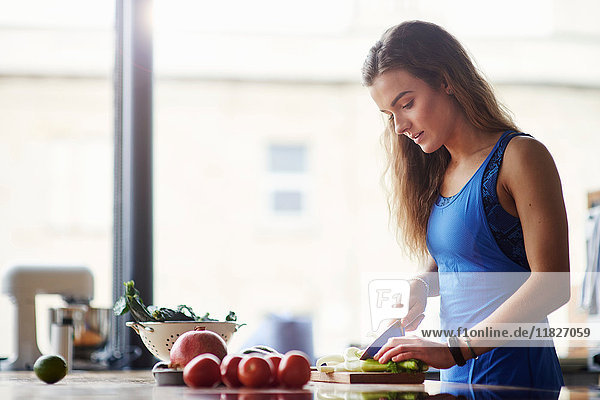 Junge Frau am Küchentisch beim Gemüseschneiden