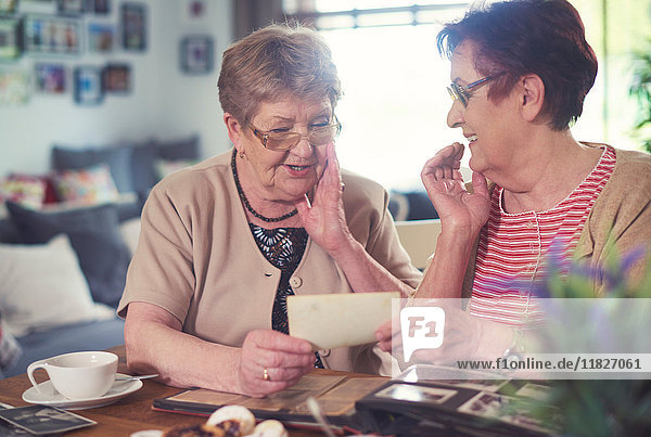 Zwei ältere Frauen unterhalten sich  während sie sich alte Fotos bei Tisch anschauen