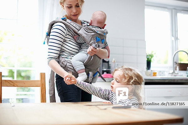 Junges Mädchen hilft Mutter beim Tischdecken  Mutter trägt Baby Junge im Tragetuch