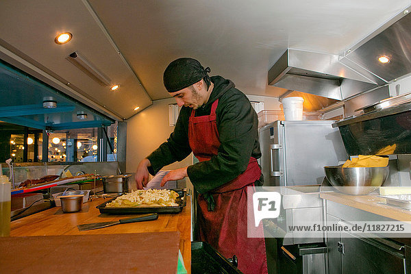 Chef preparing pizza in food stall van at night