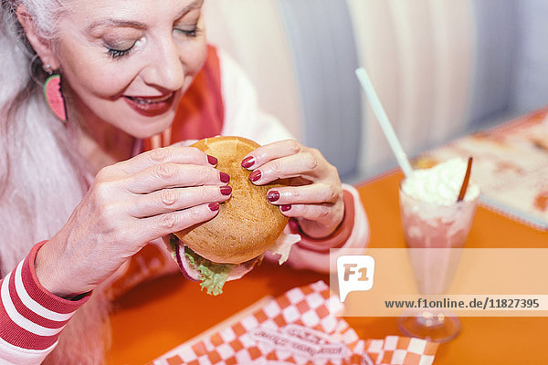 Reife Frau isst Burger im Diner der 1950er Jahre