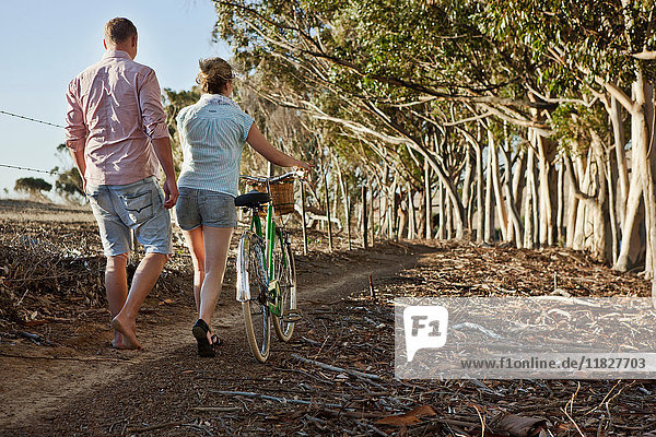 Young couple walking through woods pushing bicycle