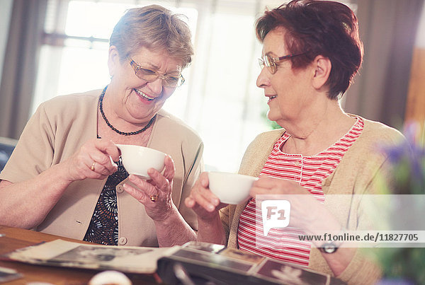 Zwei ältere Frauen lachen beim Betrachten des Fotoalbums auf dem Tisch