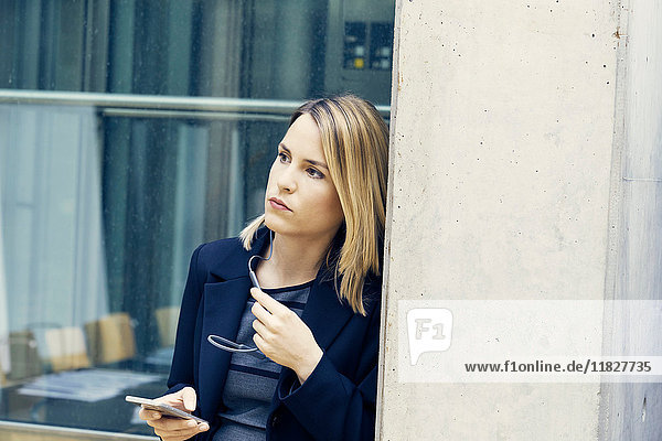 Young businesswoman leaning against office pillar gazing