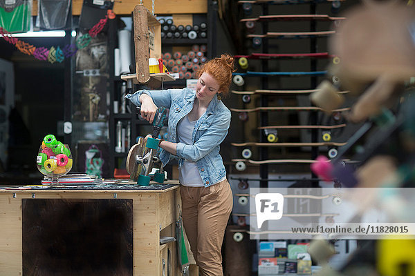 Woman working in skateboard shop  attaching wheels to skateboard