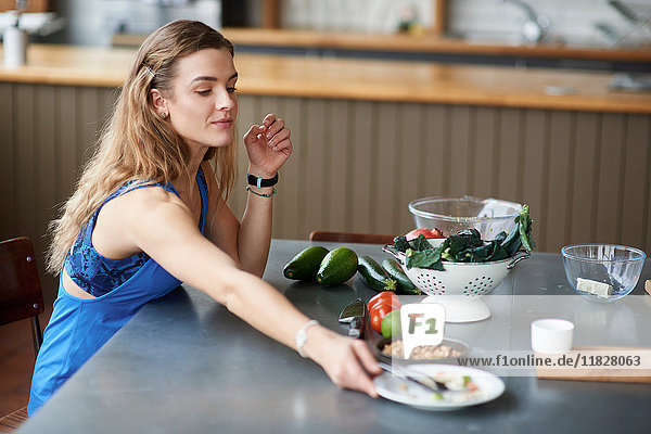 Junge Frau am Küchentisch mit fertigem Salatteller