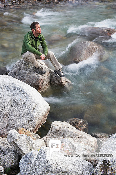 Mittelgroßer erwachsener Mann sitzt auf Felsen im Fluss