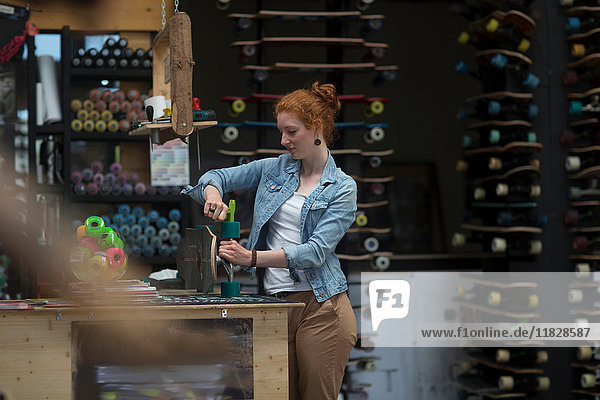 Frau  die im Skateboard-Shop arbeitet und Räder auf dem Skateboard kontrolliert