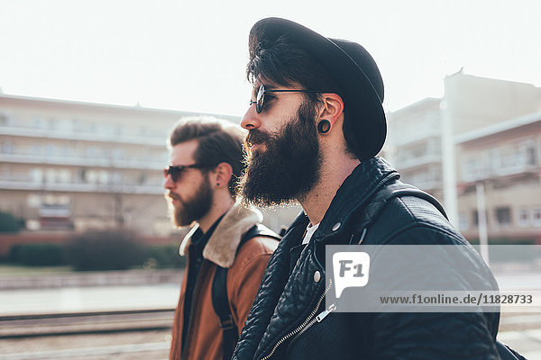 Seitenansicht von zwei jungen männlichen Hipster-Freunden mit Sonnenbrille in einer städtischen Wohnsiedlung