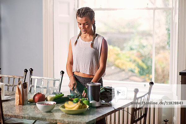 Young woman slicing cabbage at kitchen table