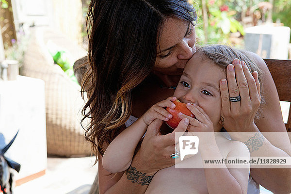 Boy eating apple with mother stroking his head