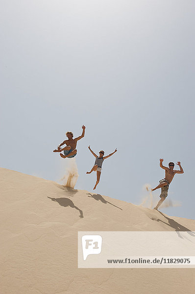 Freunde springen über eine große Sanddüne