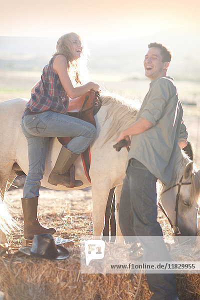 Junge Frau besteigt Pferd mit lachendem Mann