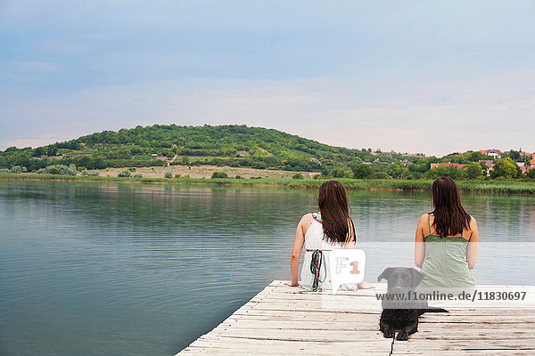 Frauen sitzen mit Hund am Pier