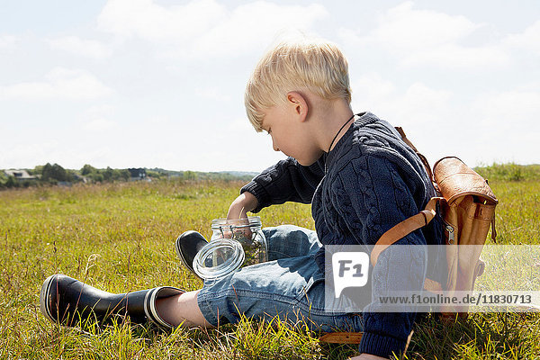 Boy filling jar in grassy field